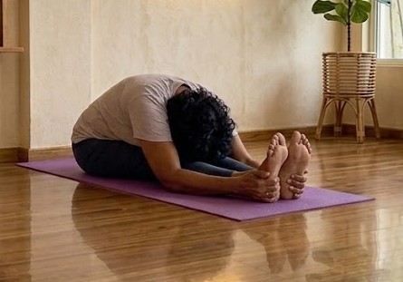 Practitioner in Paschimottanasana, a seated forward bend reaching toward the feet
