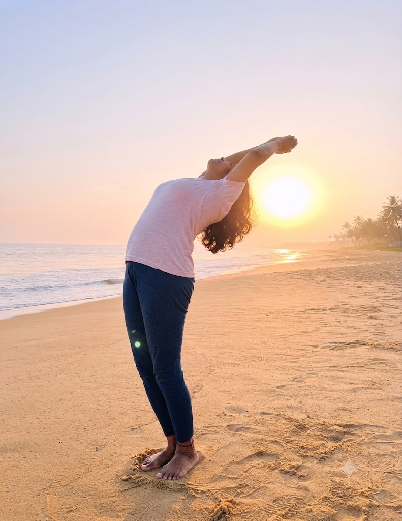 Practitioner performing a yoga sequence on a shoreline at sunrise